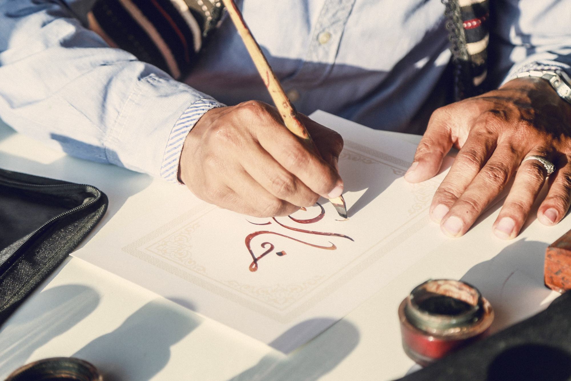 Hands writing Arabic calligraphy with a reed pen
