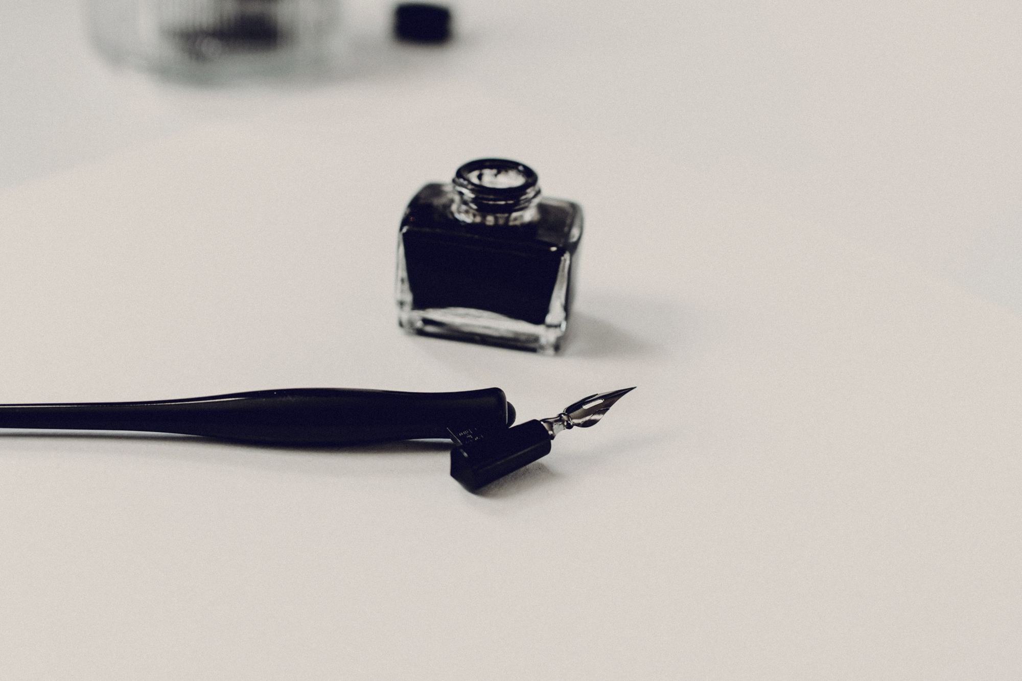 An ink bottle and dip pen on a pale surface