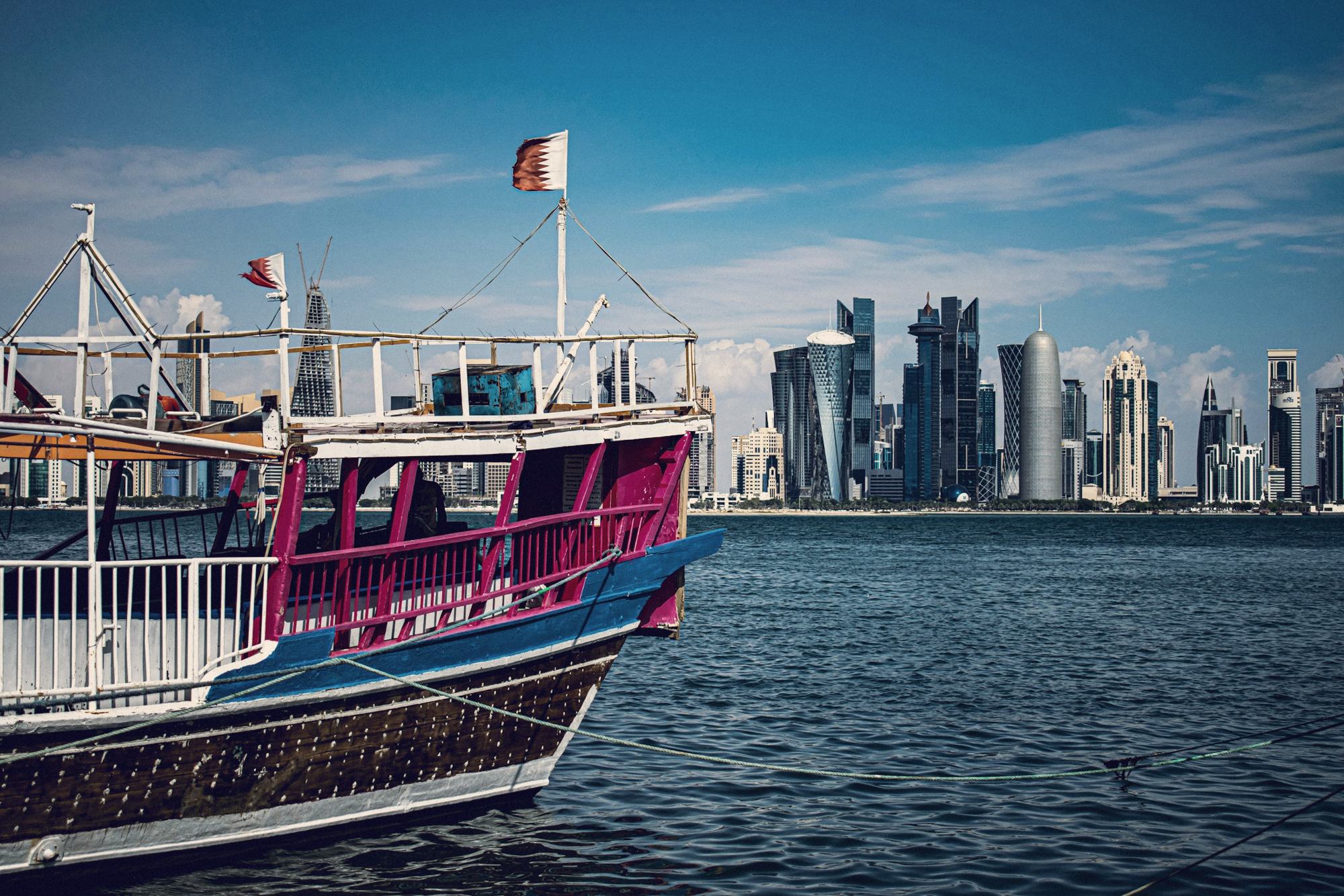 A traditional dhow flying the Qatari flag, with the West Bay towers behind
