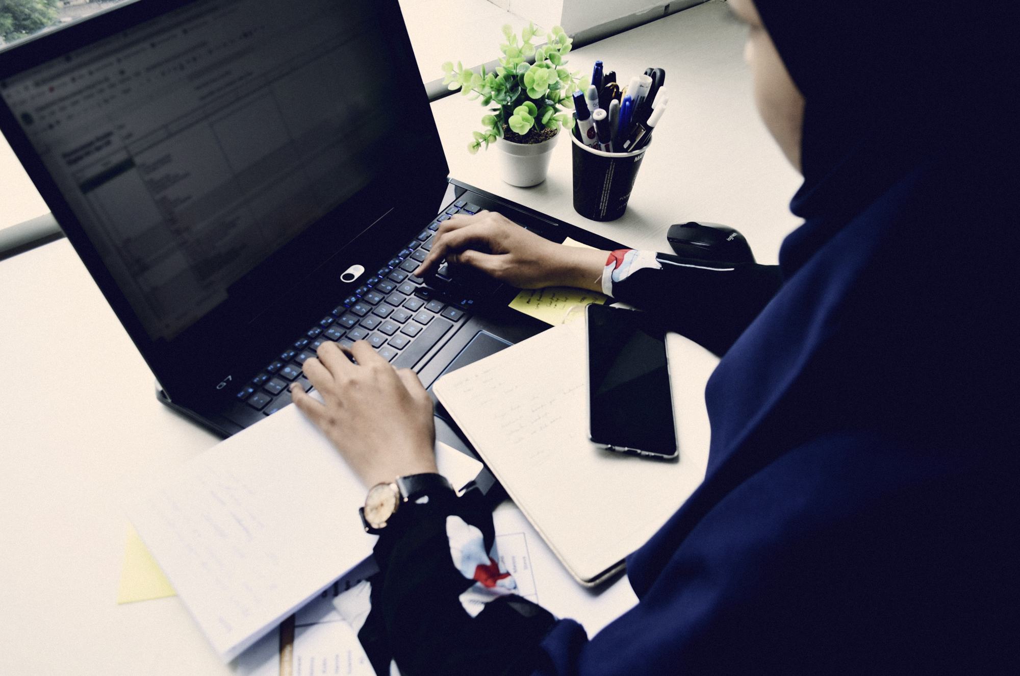 A developer in a hijab writing code on a laptop