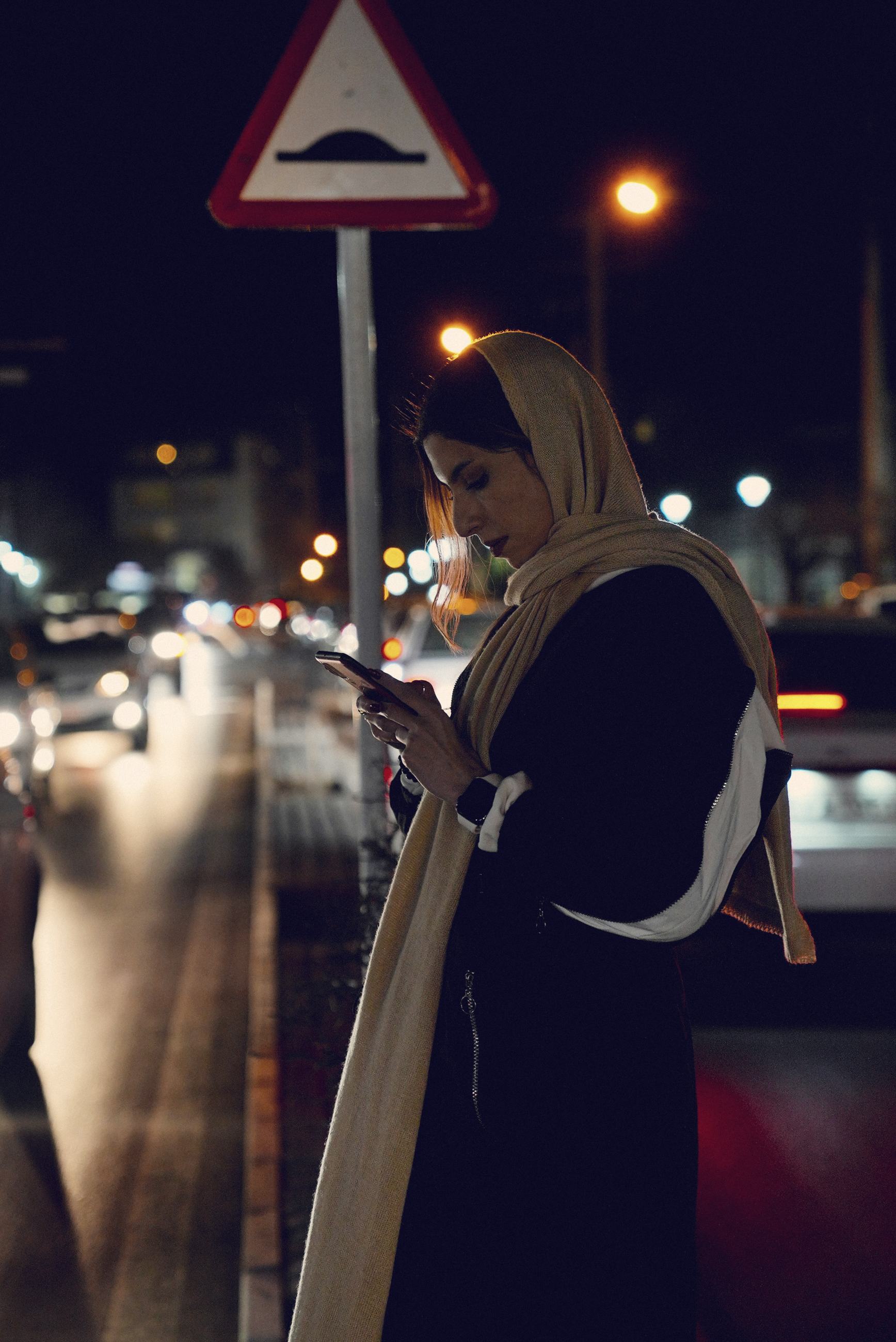 A woman in an abaya using her phone among the city lights